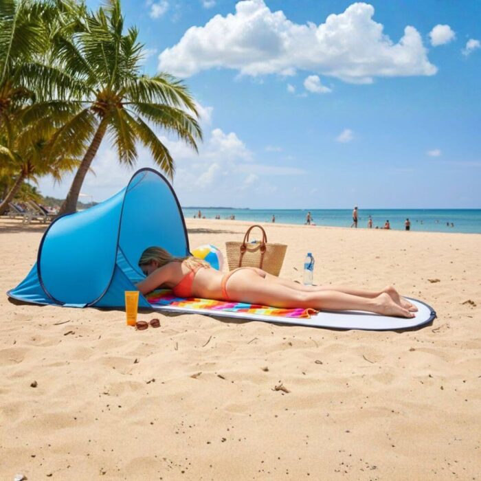 Žena leži na plavoj prostirci za plažu sa mini šatorom koji štiti glavu i lice od sunca.